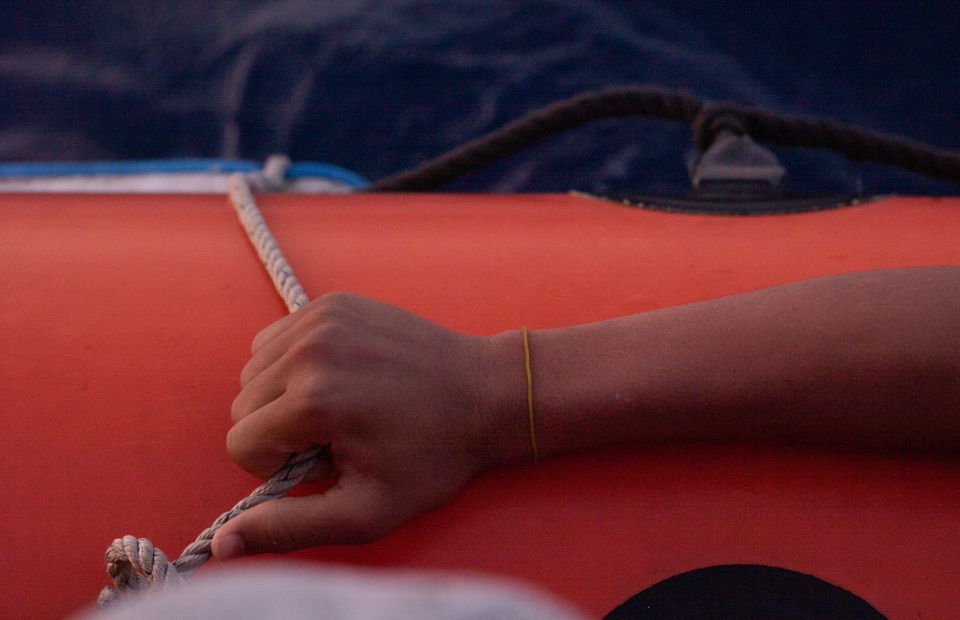 Une main tient la corde sur un canot de sauvetage rouge.